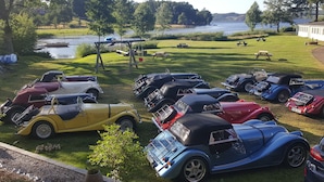 Un espace de stationnement où sont exposées des voitures anciennes, avec des tables de pique-nique et une vue sur le lac.