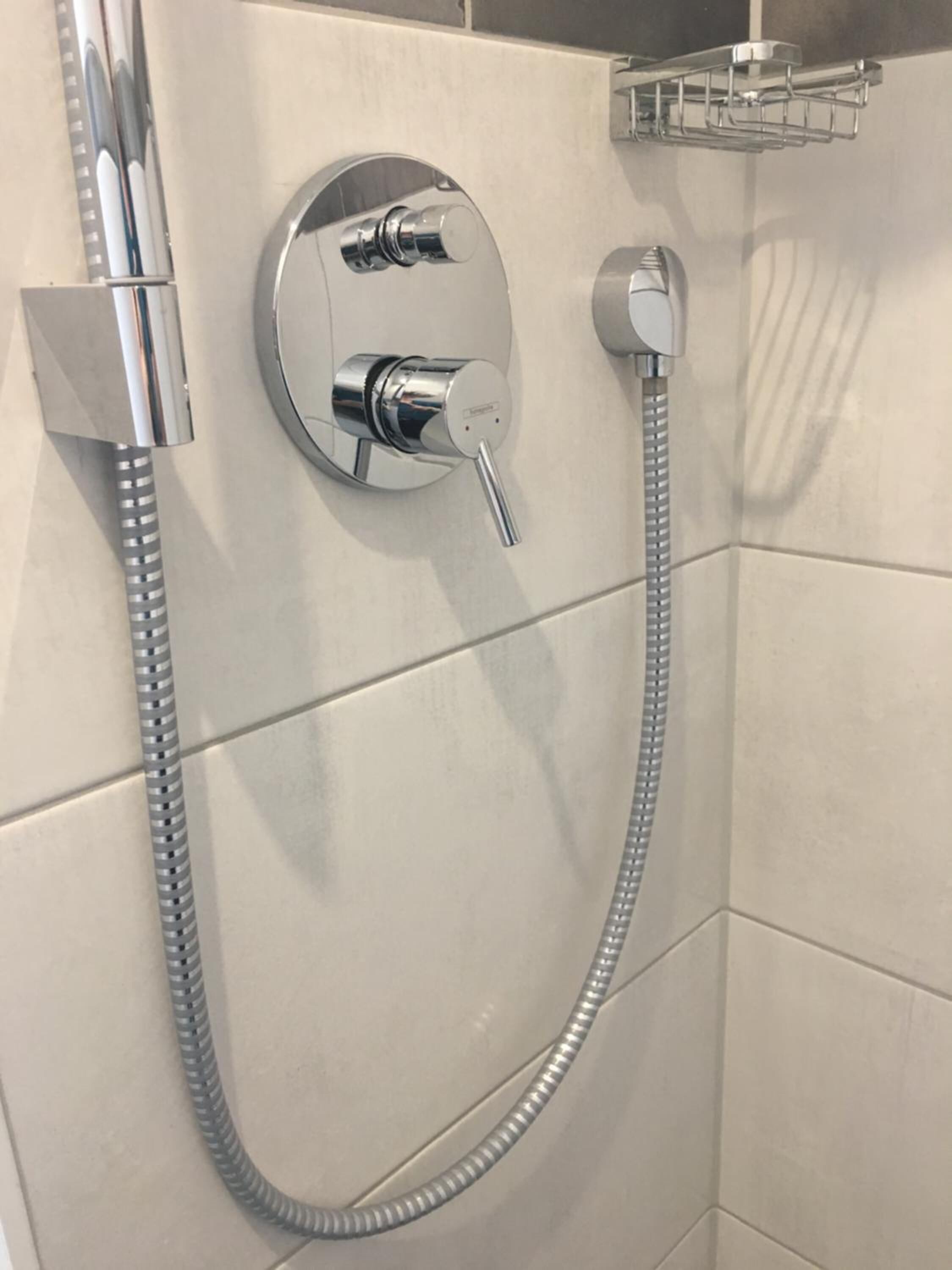Une douche équipée d’un pommeau de douche à main et d’un pommeau de douche fixe, tous deux fixés au mur et dotés d’une finition chromée.