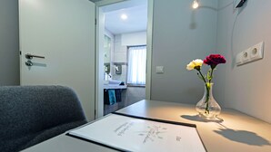 A hotel room with a desk, a vase with flowers, and a view of the bathroom and kitchen. - Haus Mittelrhein (Rhens)