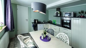 A modern kitchen with white cabinets, a built-in microwave, and a dining area with a table and chairs. - Haus Mittelrhein (Rhens)