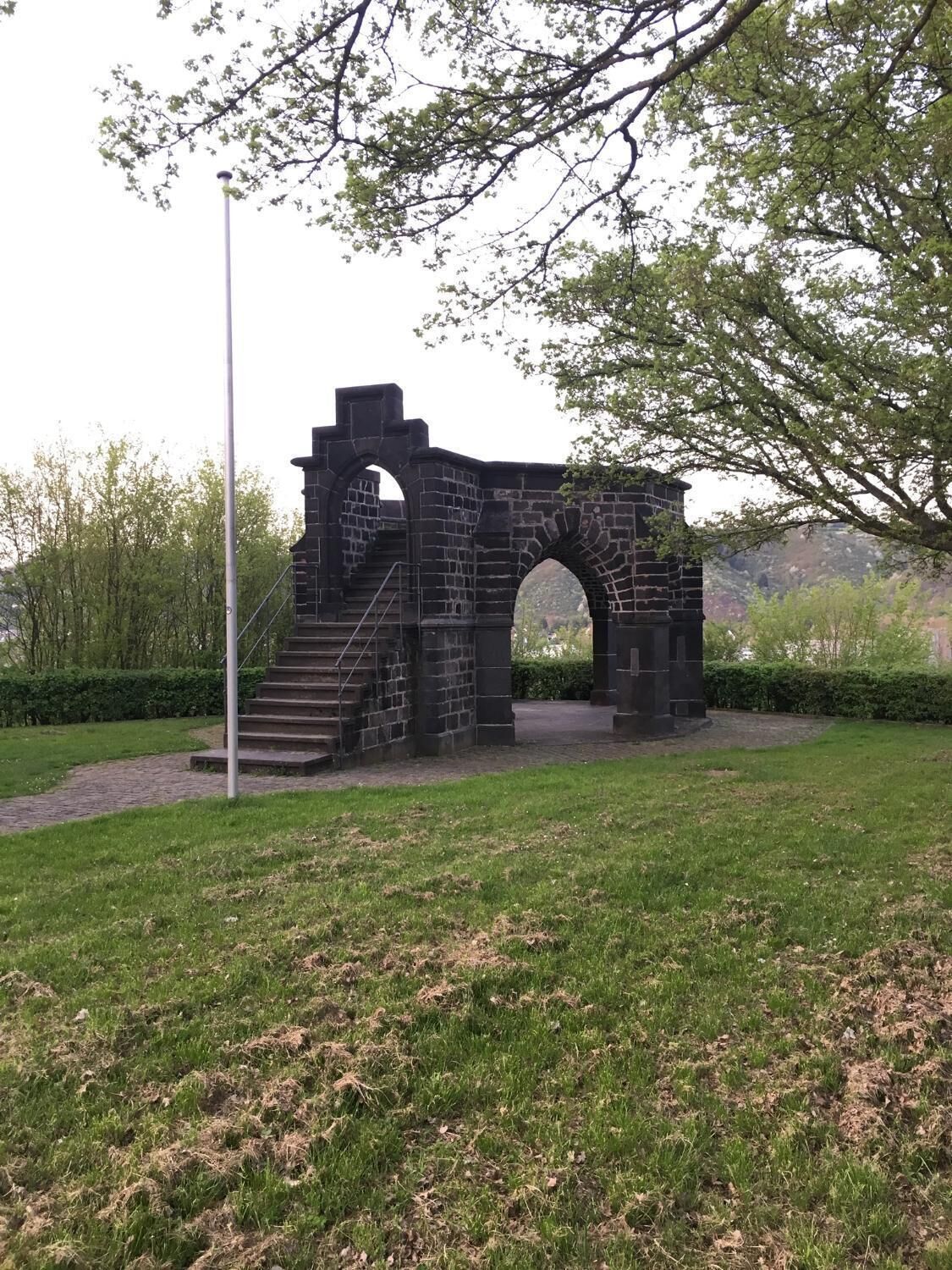 Una estructura de piedra con un arco y una escalera que lleva a ella, rodeada de césped y árboles.