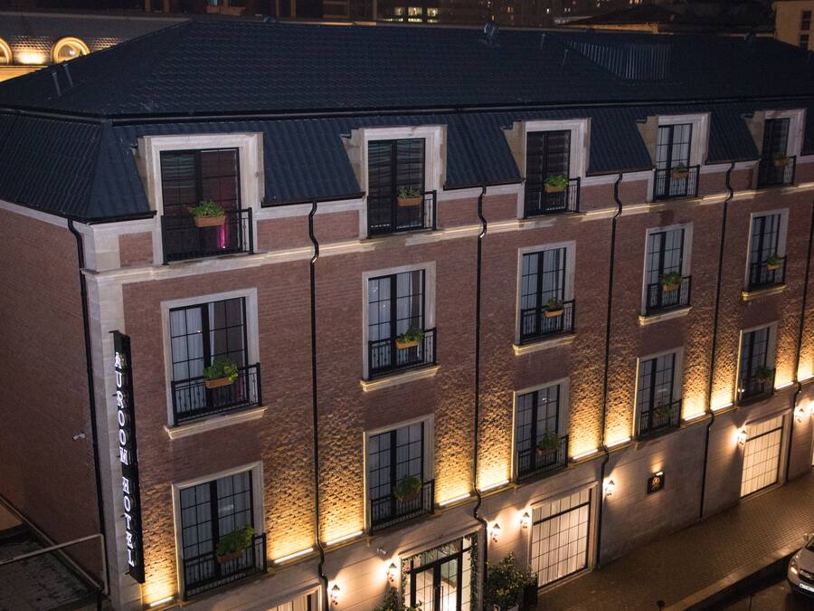 Un hotel a più piani con facciata in mattoni, diversi balconi con piante in vaso e un esterno ben illuminato.