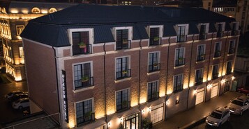 Un hotel de varios pisos con fachada de ladrillo, múltiples balcones con macetas y un exterior bien iluminado.