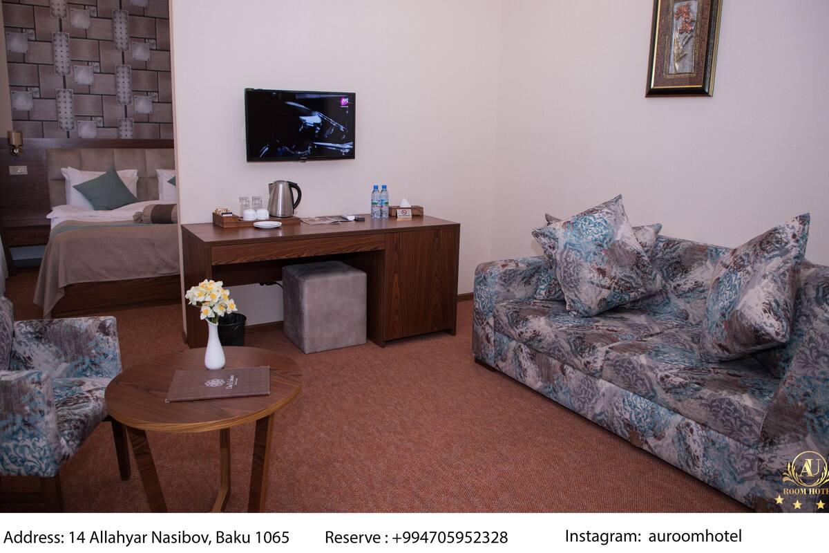 Een hotelkamer met een bed, een bureau, een bank en een televisie. Op het bureau staat een vaas met bloemen.