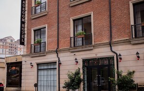 Fachada de hotel con paredes de ladrillo, amplias ventanas y plantas exteriores.