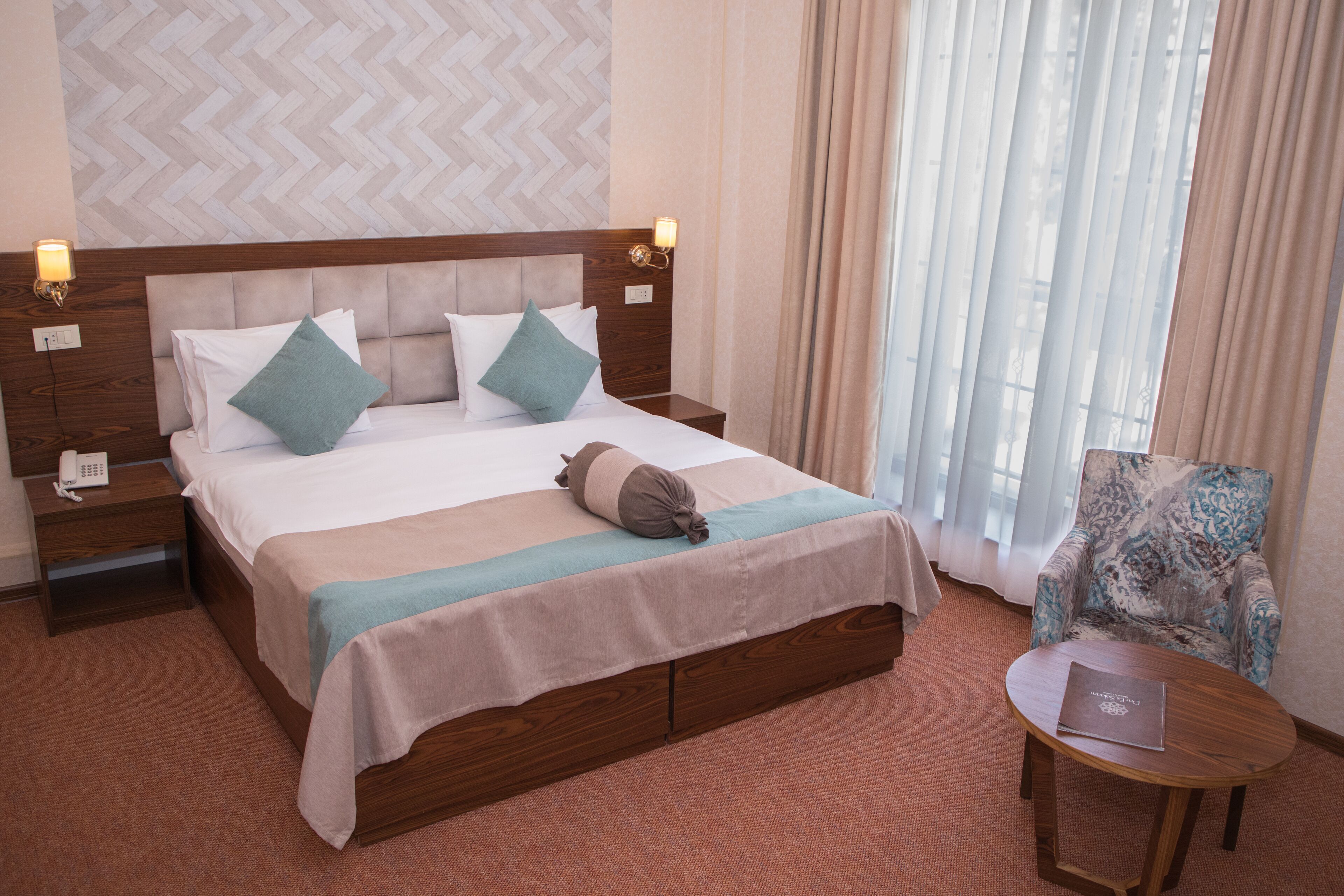 Habitación de hotel con una cama grande, dos mesitas de noche, una silla y una pequeña mesa.