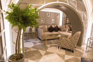 A modern living room with a sectional sofa, patterned armchairs, a coffee table, and a potted tree. - Theatrum Hotel Baku (Baku)