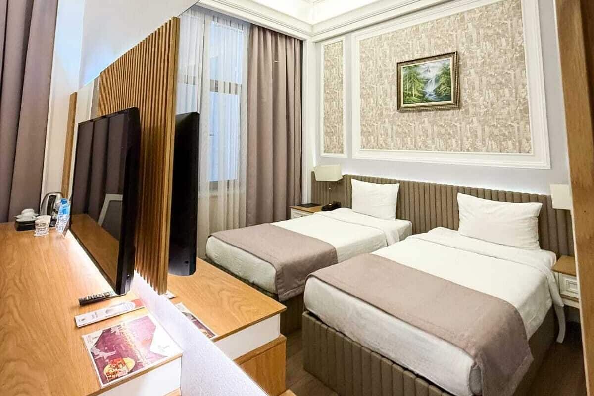 A hotel room with two beds, a desk, a television, and a painting on the wall.