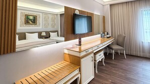 A hotel room with a wooden bench, a TV mounted on the wall, a desk with drawers, a chair, and a bed with white linens. - Theatrum Hotel Baku (Baku)