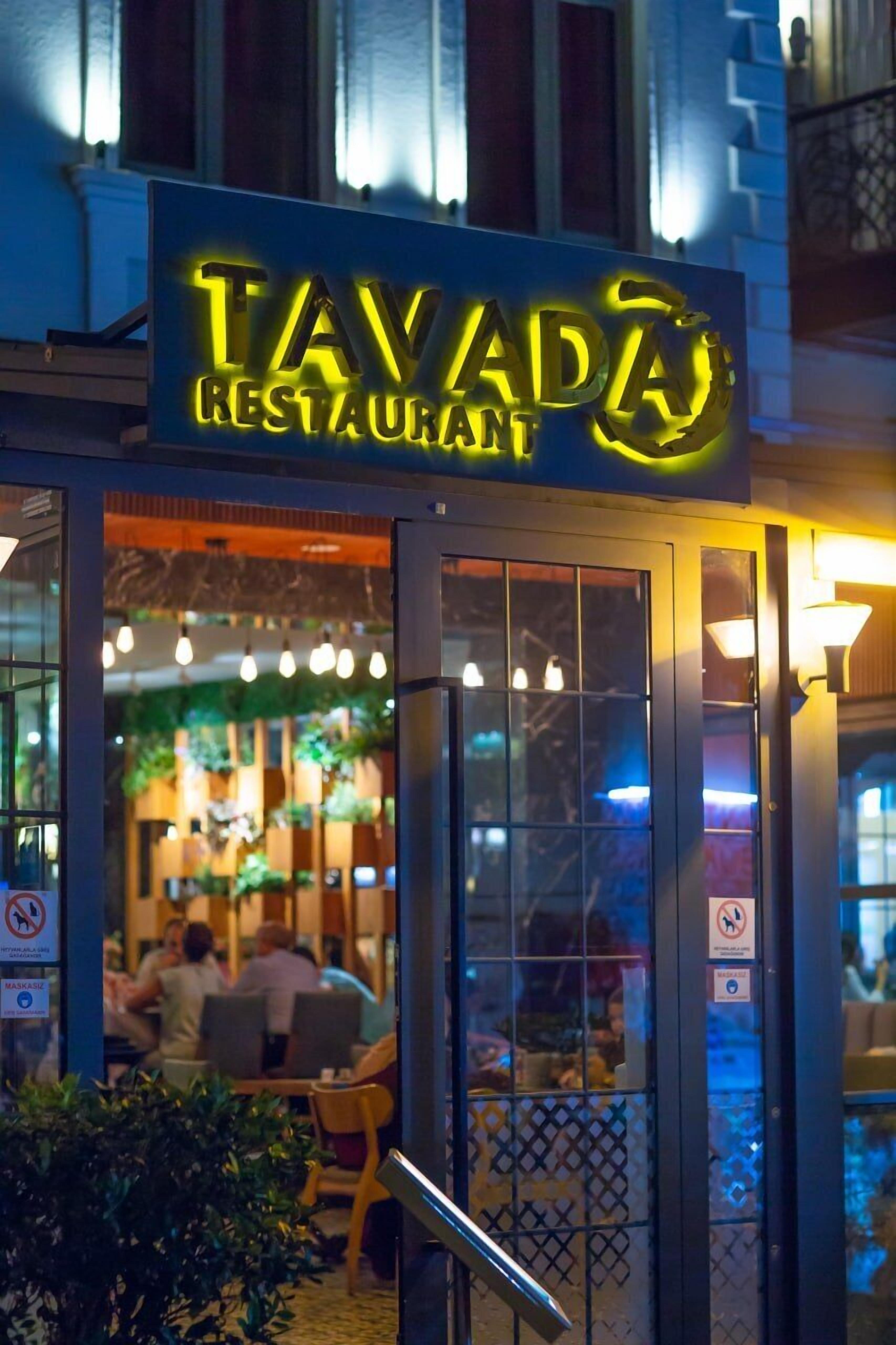 A restaurant sign with the name 'TAVADA RESTAURANT' illuminated at night.