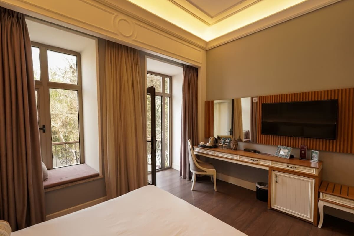 Una habitación de hotel con una cama grande, un escritorio con silla, televisión y una ventana con cortinas.