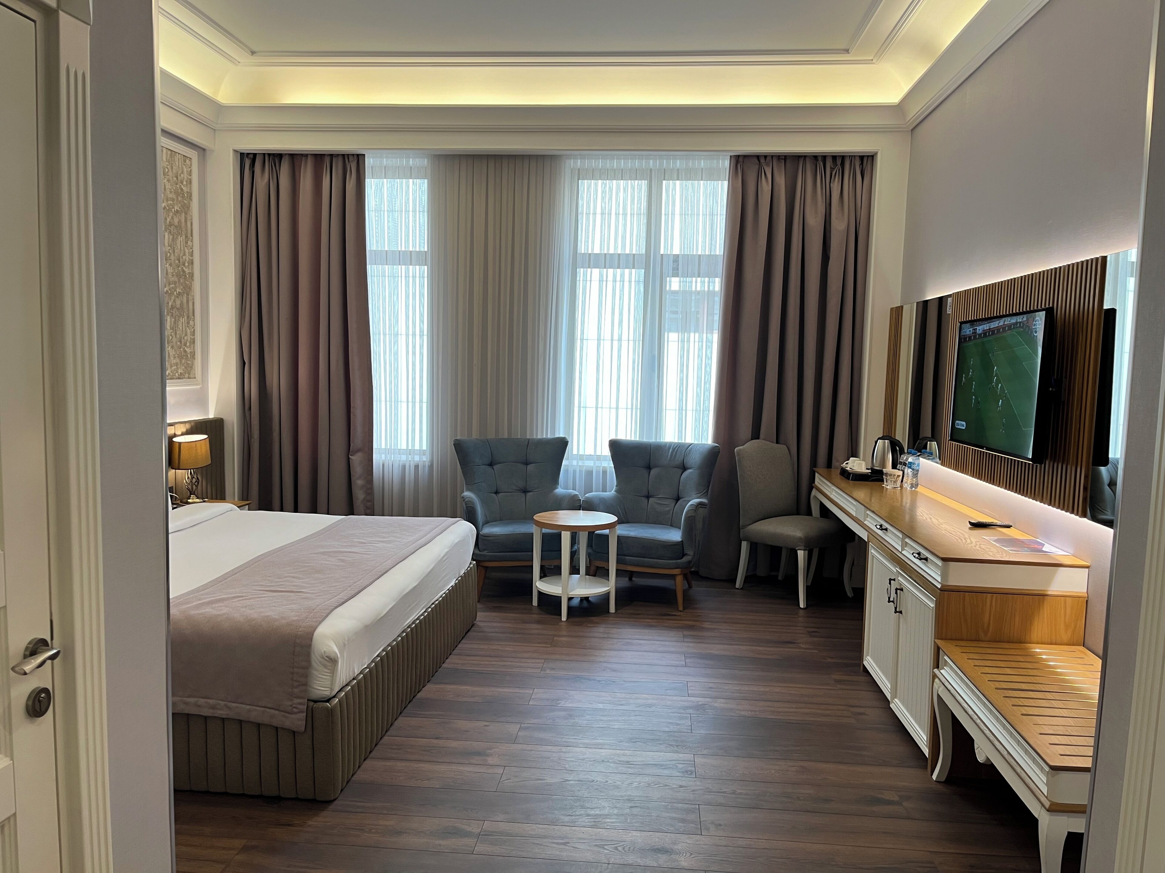 A hotel room with a bed, a desk, a TV, and a seating area with chairs.