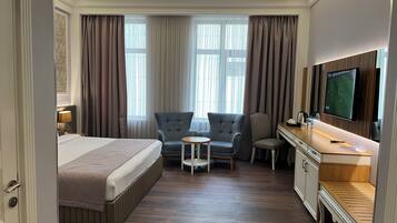 A hotel room with a bed, a desk, a TV, and a seating area with chairs.