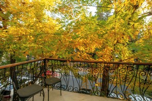 A balcony with a wrought iron railing, a chair, and a view of trees with yellow leaves.