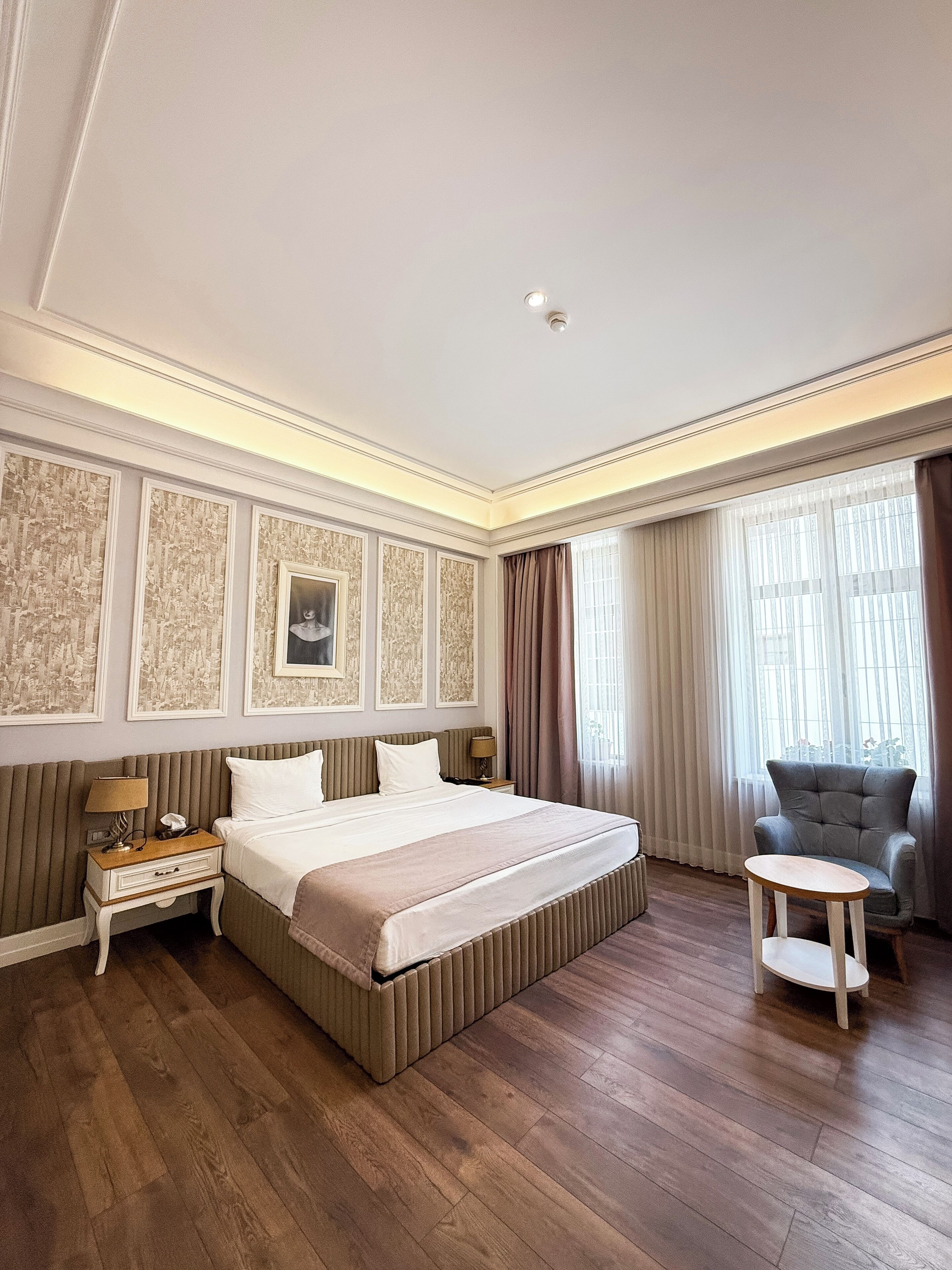 Ein geräumiges Hotelzimmer mit einem großen Bett, einem Nachttisch mit Lampe, einem Sessel und Blick auf die Stadt durch das Fenster.