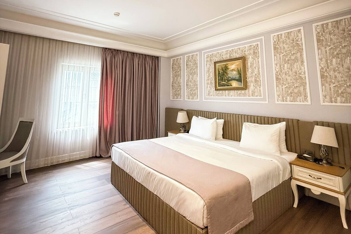 A hotel room with a large bed, a chair, a nightstand, and a window with curtains.