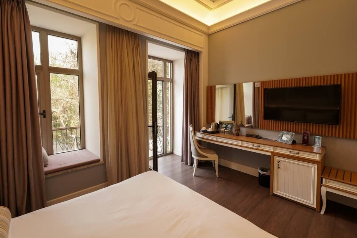 Een hotelkamer met een groot bed, een bureau met stoel, een televisie en een raam met gordijnen.