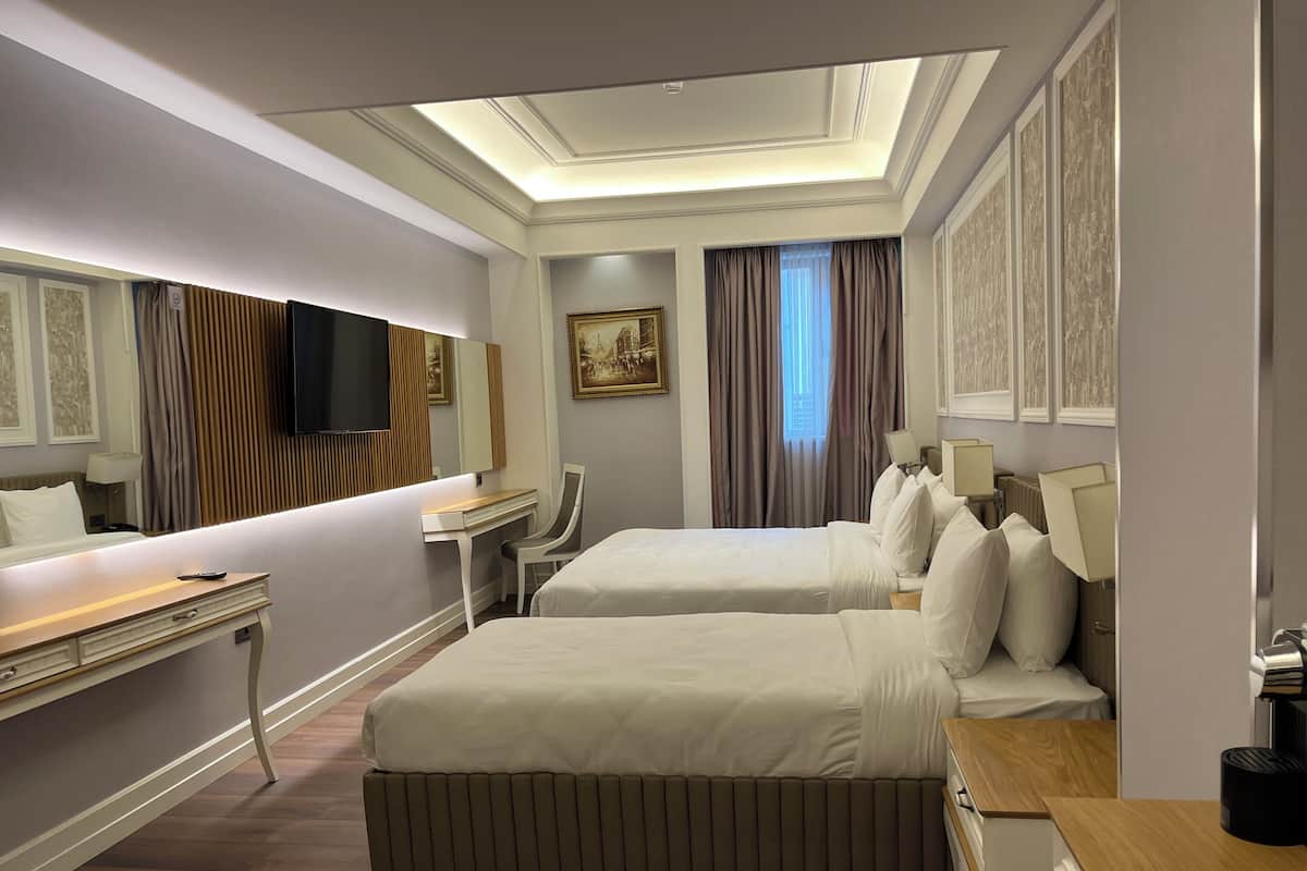 A hotel room with two beds, a desk, a chair, a television, and a painting on the wall.