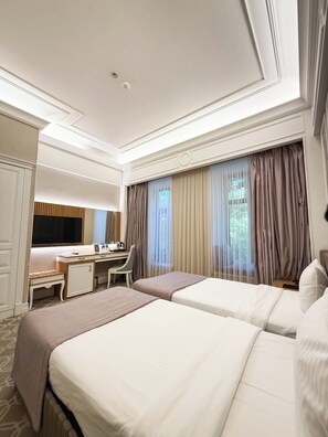A hotel room with two beds, a desk, a chair, a television, and a large window with curtains.