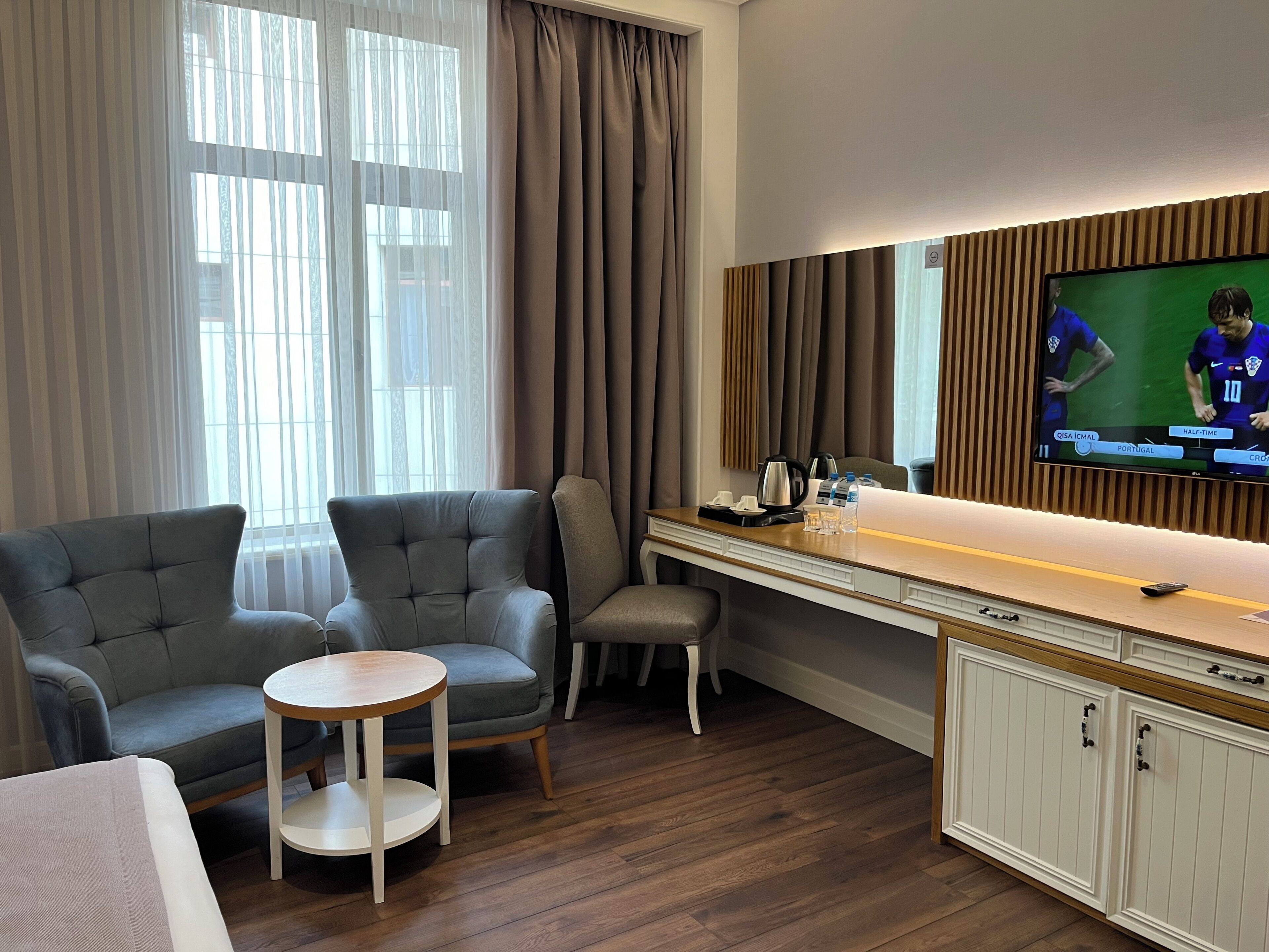 A hotel room with a seating area, a desk, a television, and a window with curtains.