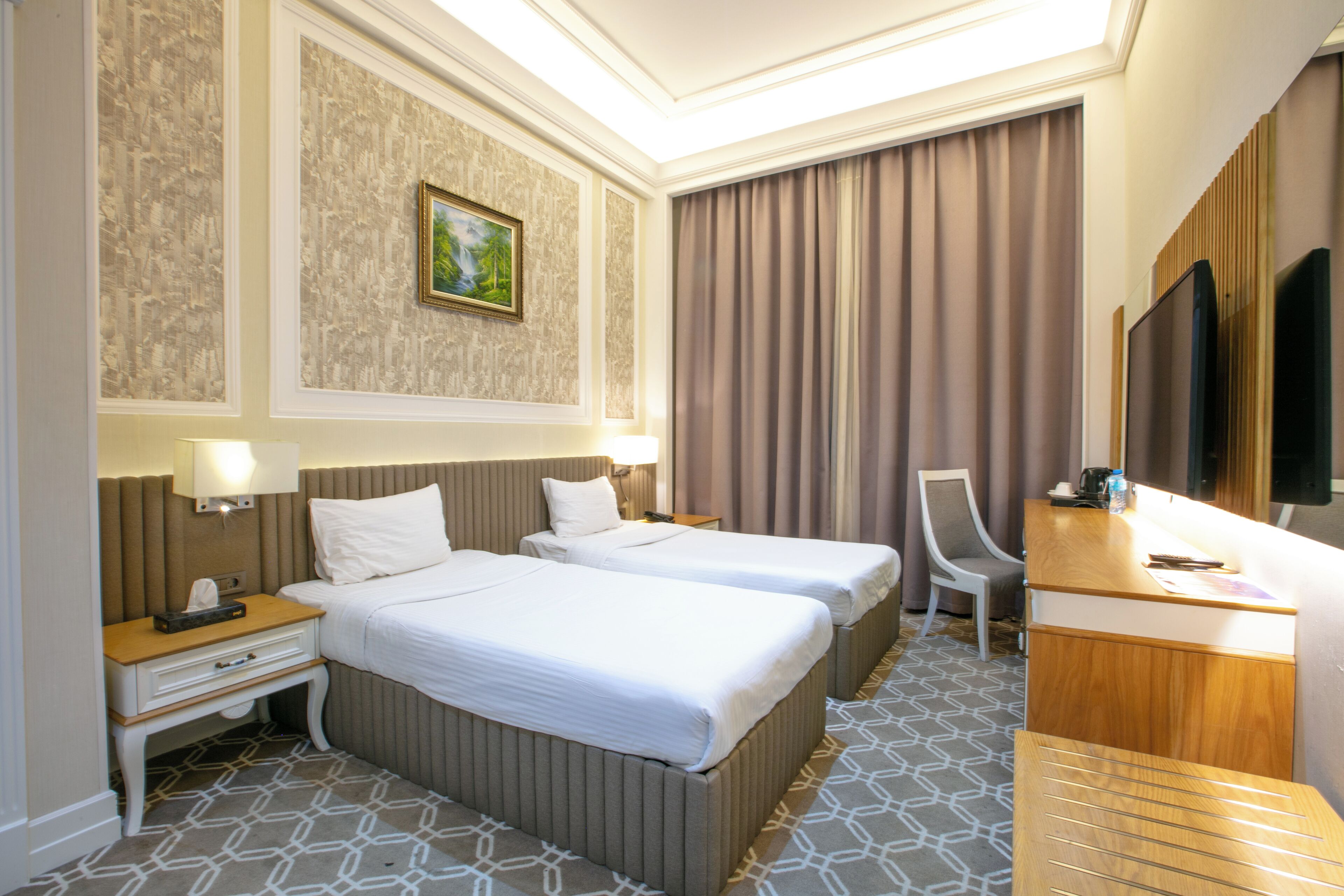 Une chambre d’hôtel avec deux lits, un bureau, une chaise, une télévision et un tableau au mur.