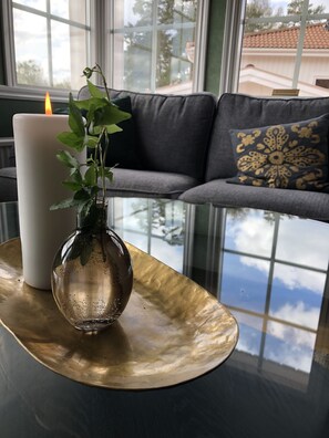 Una mesa con una vela, un jarrón de cristal con una planta y un cojín decorativo en un sofá.
