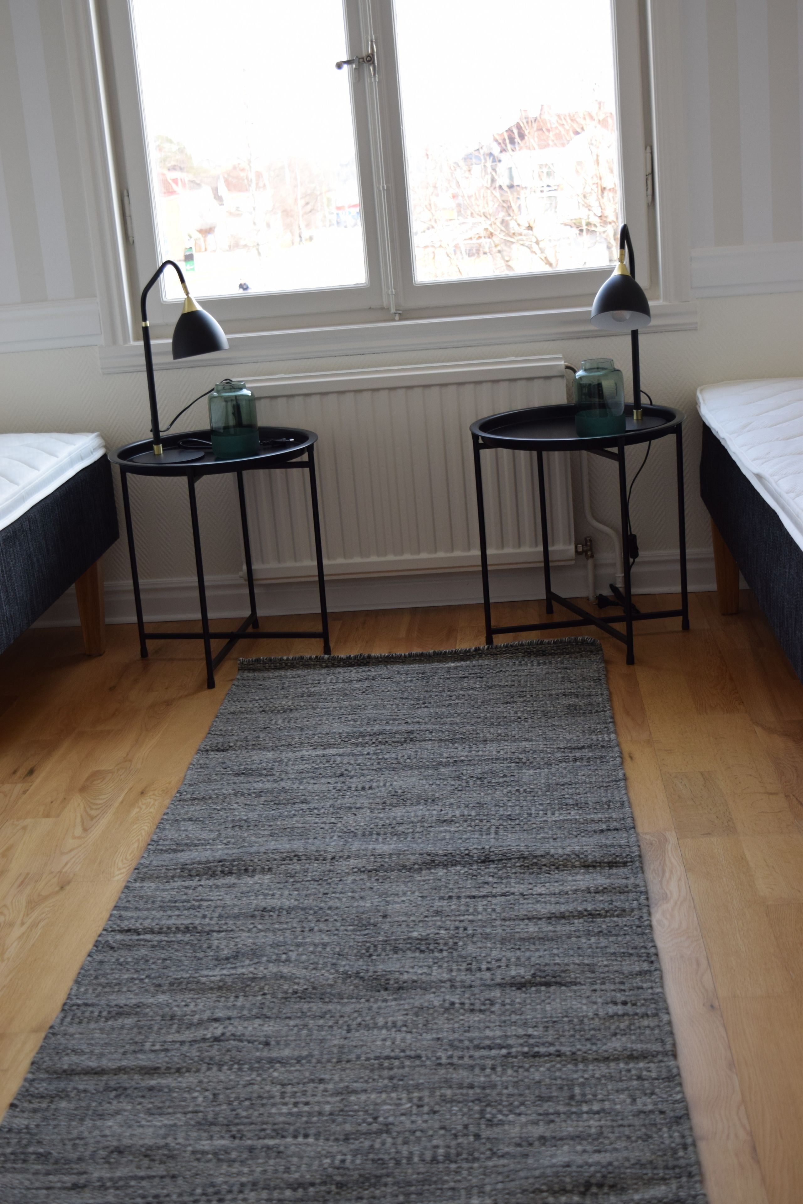 A room with two beds, a gray rug, and two black side tables with lamps.