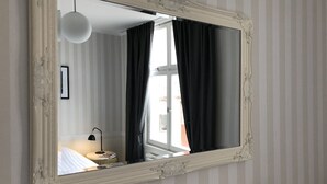 A hotel room with a large ornate mirror, striped wallpaper, a round table with a lamp, and a view of the outdoors through a window with black curtains.