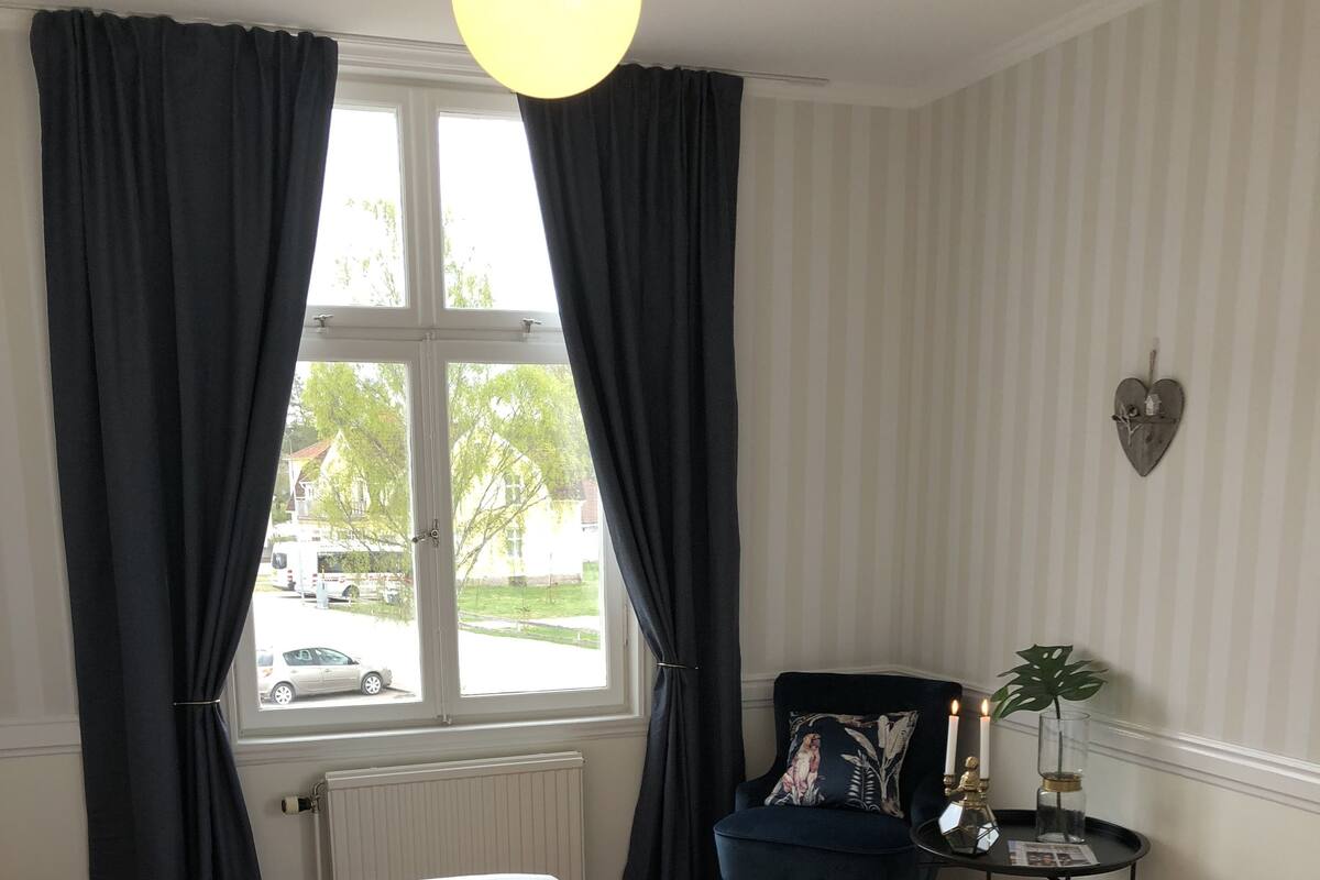 Un dormitorio con dos camas, una ventana con cortinas, una mesita con una planta y una decoración de corazón en la pared.