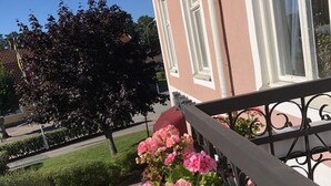 A balcony with pink flowers, a clear sky, and a building with windows in the background.