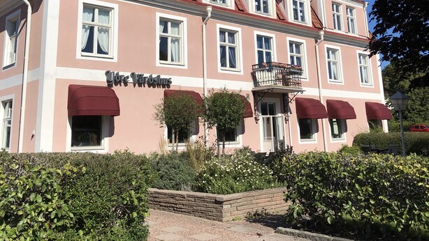 A pink building with multiple windows and a sign that reads "Hotel Vardishus".