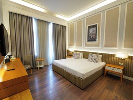 Een hotelkamer met een groot bed, een bureau, een stoel, een televisie en een raam met gordijnen.