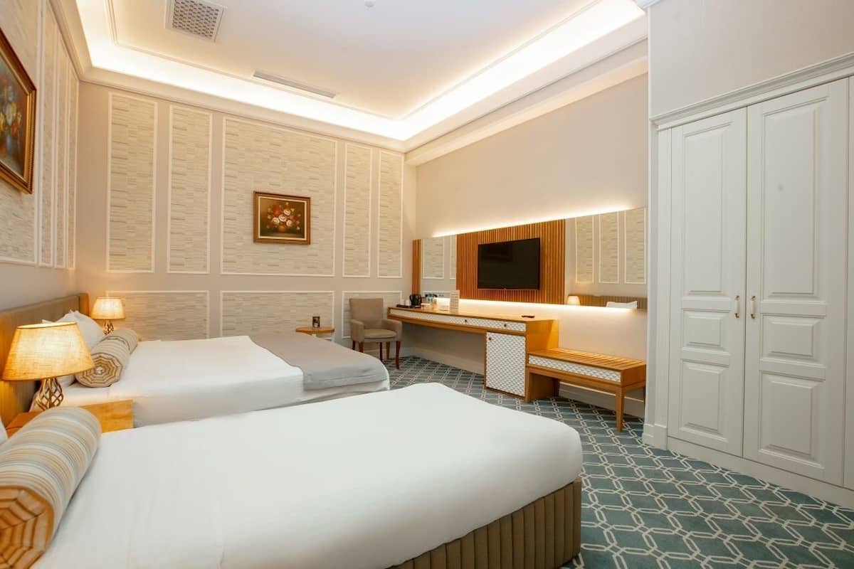 A hotel room with two beds, a desk, a chair, a TV, and a wardrobe.