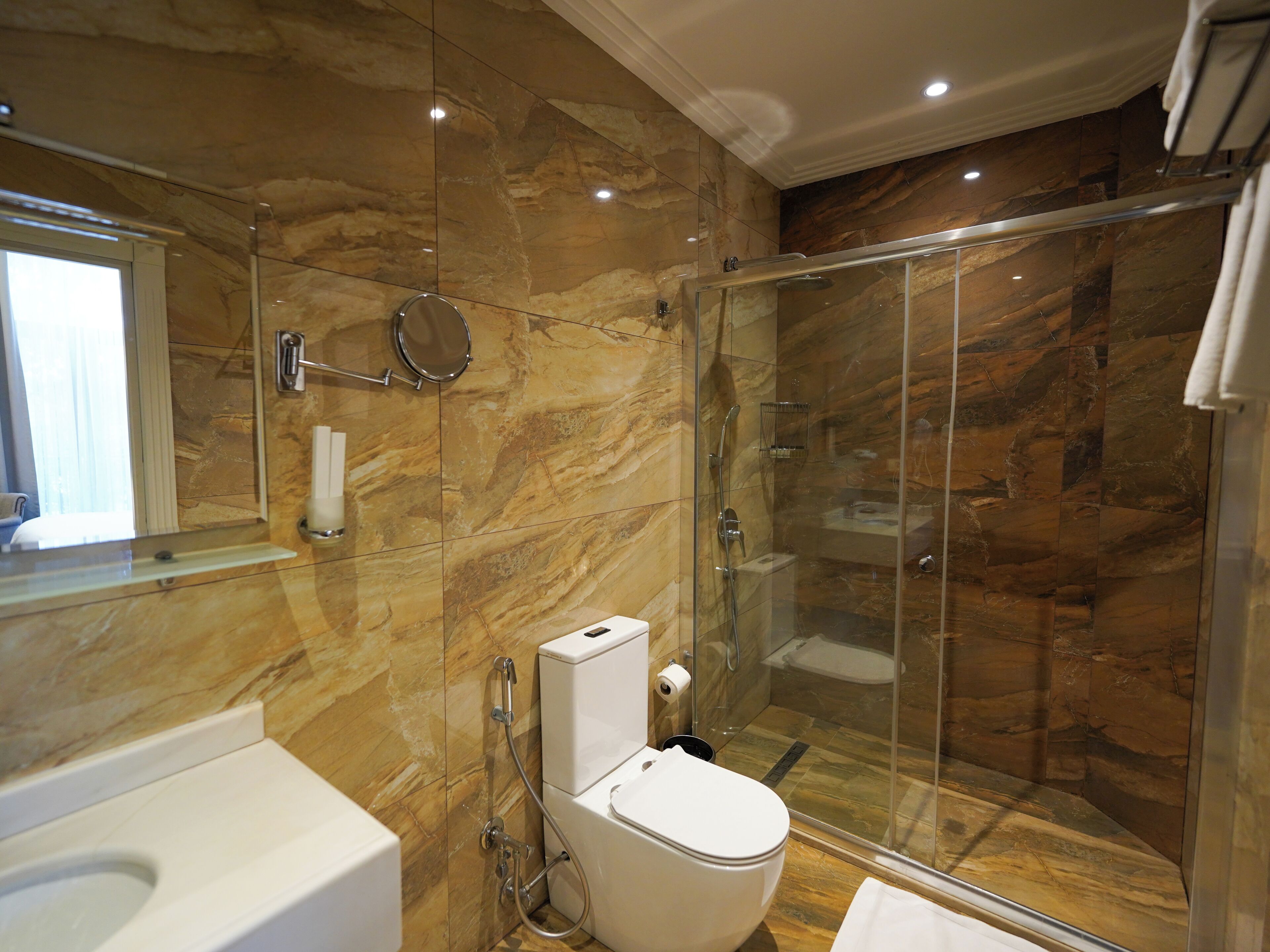 Ein modernes Badezimmer mit einer gläsernen Duschkabine, einer weißen Toilette und einer Marmorwand.