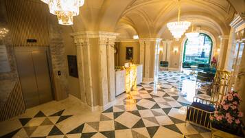 A hotel lobby with a check-in counter, elevators, and a check-out desk.