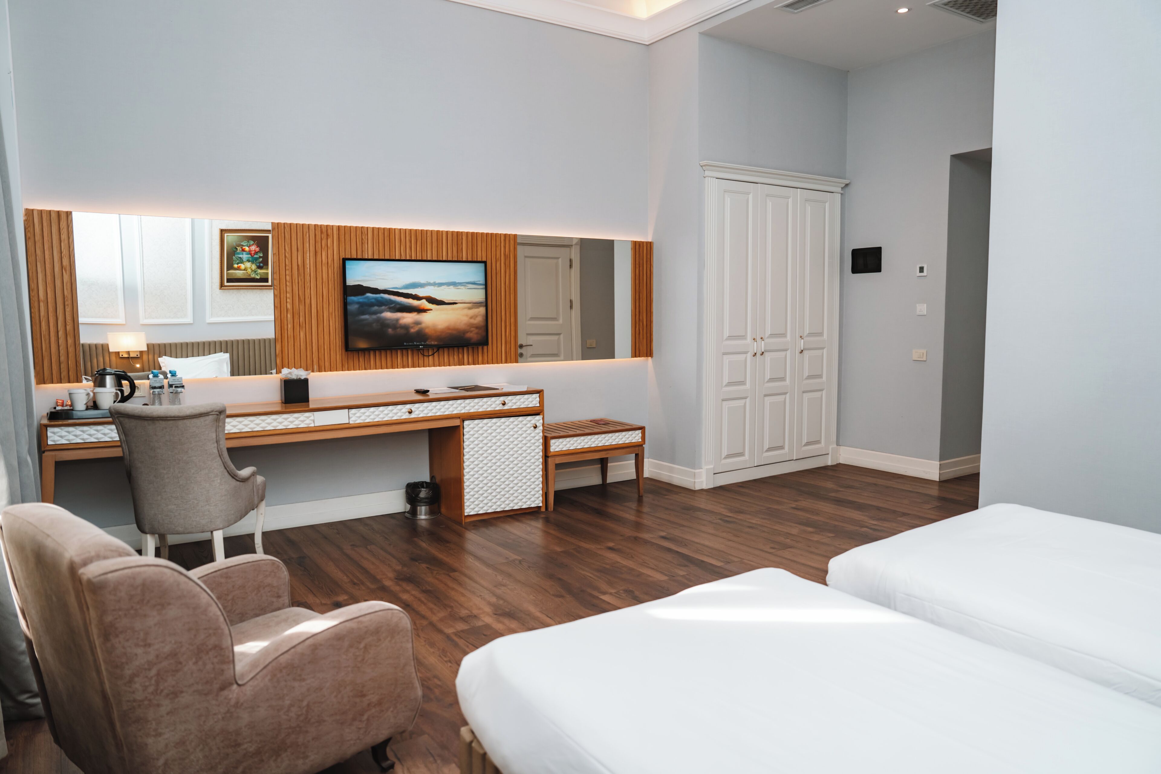 A hotel room with a wooden desk, a television, a bed, and a wardrobe.