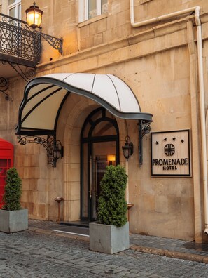 The entrance of the Promenade Hotel with a covered entrance, a signboard, and two potted plants. - Promenade Hotel Baku (Baku)