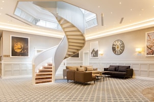Een ruime lobby met een moderne spiraaltrap, comfortabele zithoeken en een grote wandklok.