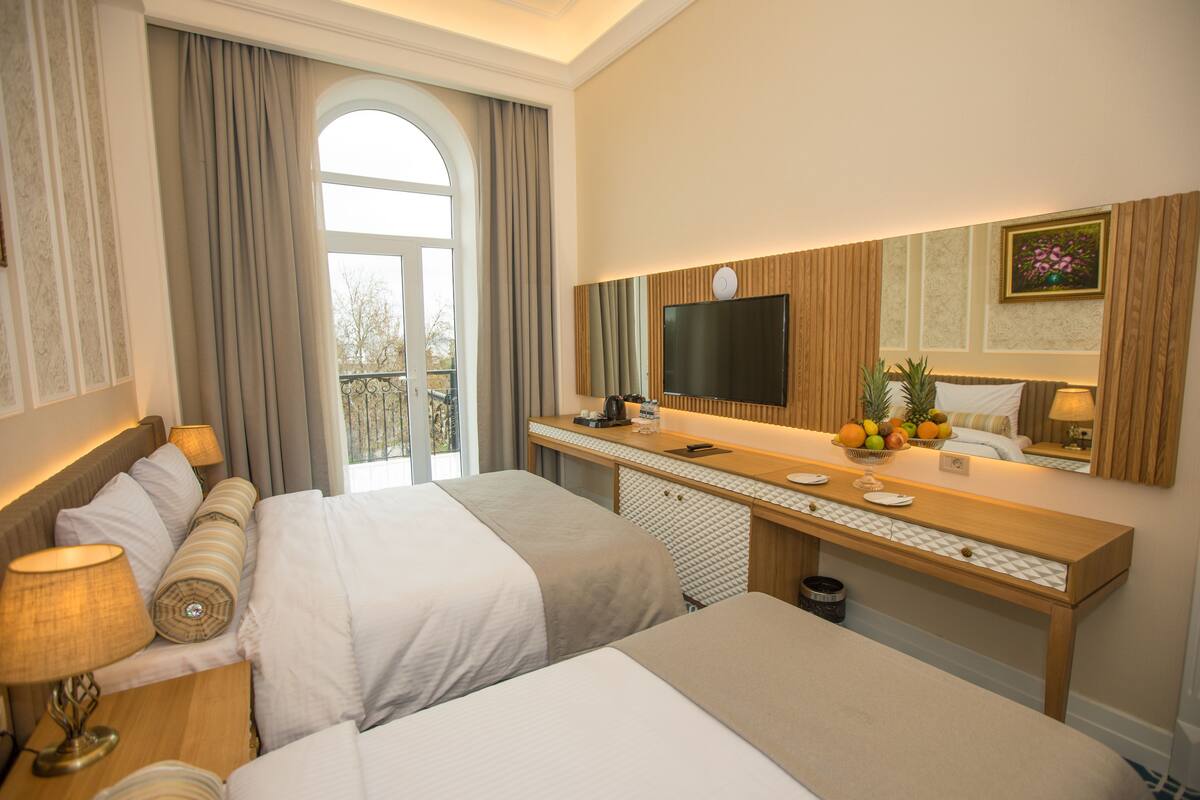 A hotel room with two beds, a desk with a computer, a TV, and a window with curtains.