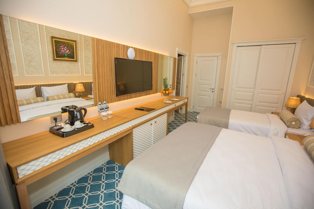 A hotel room with a large bed, a desk with a flat-screen TV, a mirror, and a door.
