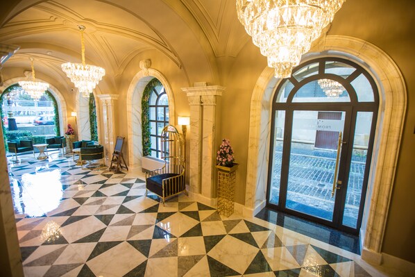 A hotel lobby with a checkered floor, arched windows, chandeliers, and a view of the street outside. - Promenade Hotel Baku (Baku)