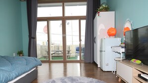 A bedroom with a bed, a TV, a refrigerator, and a view through a glass door to an outdoor area. - Gangneung Ocean Marina Pension - Hostel (Gangneung)