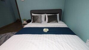 A neatly made bed with a white and blue bedspread, two decorative pillows, and a small bouquet of white flowers in the center. - Gangneung Ocean Marina Pension - Hostel (Gangneung)