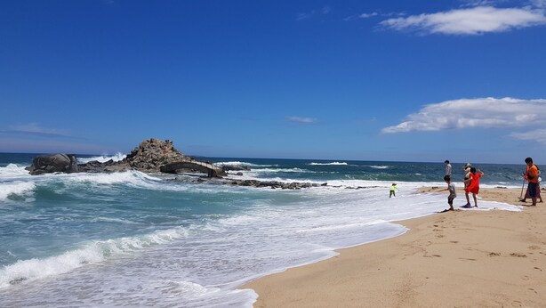 A beach with waves, a rocky outcrop, and people on the sand. - Gangneung Ocean Marina Pension - Hostel (Gangneung)