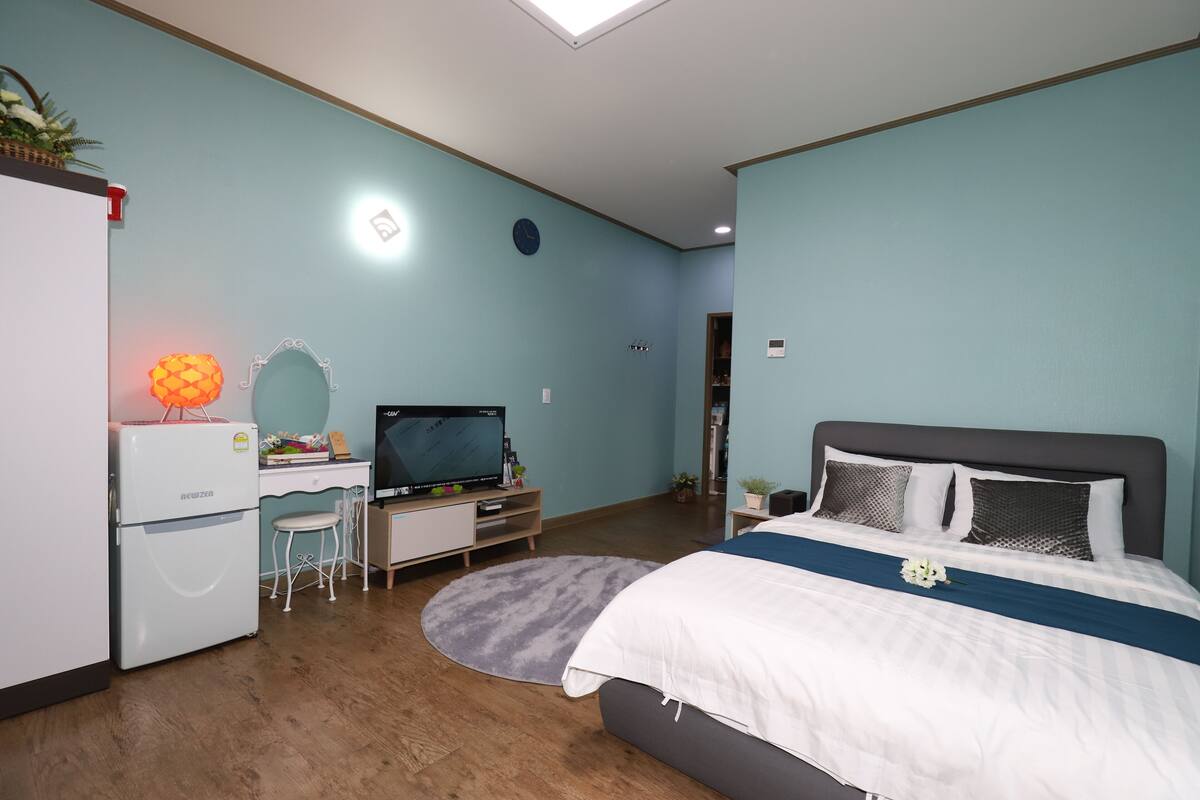 A bedroom with a bed, a desk, a refrigerator, and a television.