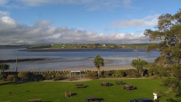 A coastal view with a grassy area, picnic tables, and a small structure. - Courtmacsherry hotel (Courtmacsherry)
