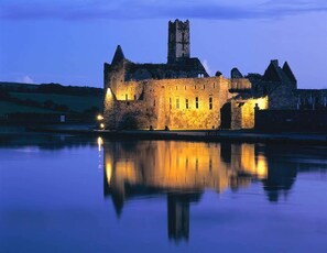 A historic stone castle with a prominent tower, situated by a calm body of water reflecting its structure. - Courtmacsherry hotel (Courtmacsherry)