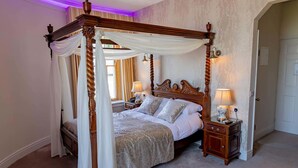 A four-poster canopy bed with a wooden frame and draped white curtains, two bedside tables with lamps, and a view of a door in the background. - Courtmacsherry hotel (Courtmacsherry)
