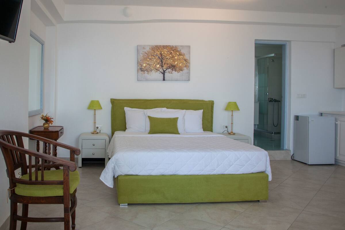 A bedroom with a bed, bedside tables, a chair, a TV, and a painting of a tree.