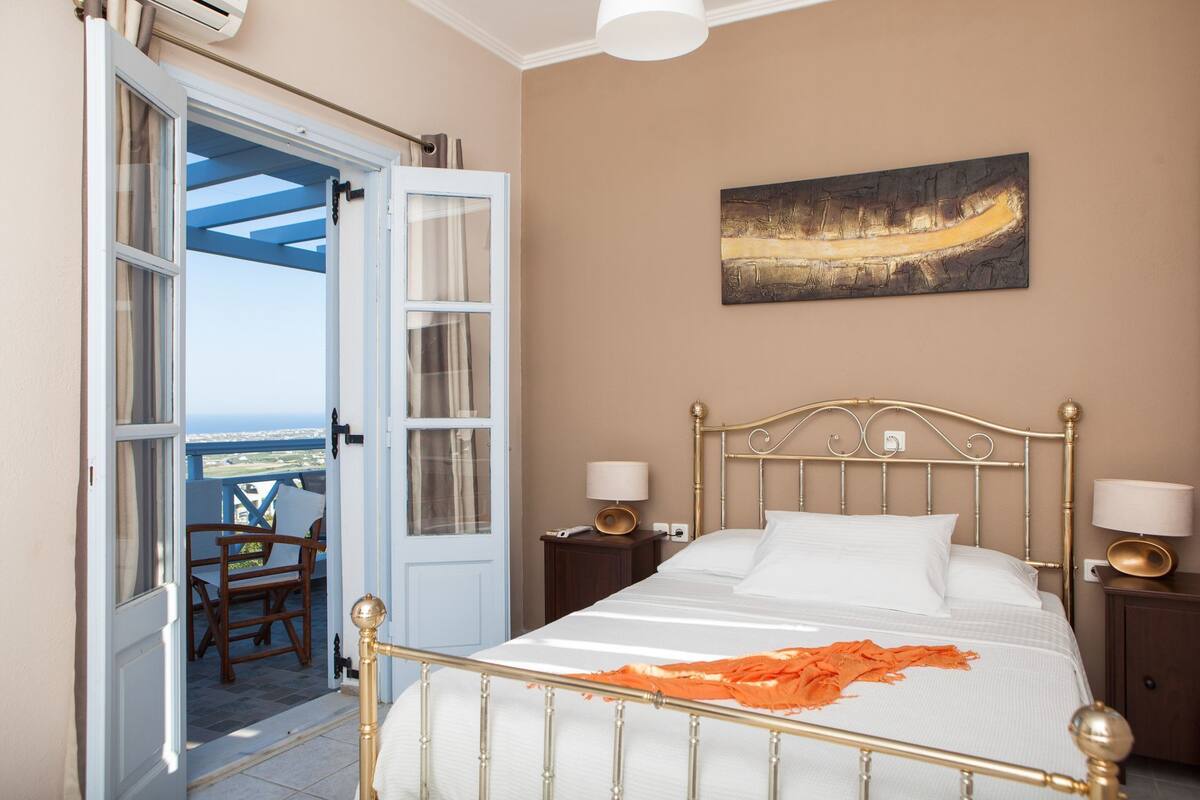 A bedroom with a bed, bedside lamps, a painting, and a view through an open door.